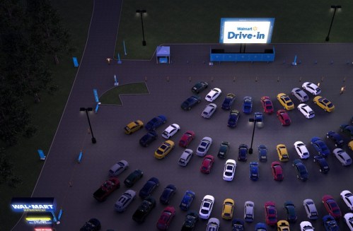 Aerial view of a Walmart drive-in event with cars parked in a lot and a large screen displaying "Drive-in."