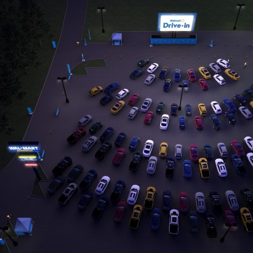 Aerial view of a Walmart Drive-In event with numerous cars parked in rows and a large screen displaying the Walmart logo.