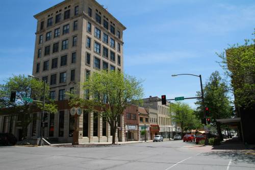 A city street view featuring a tall building, green trees, and traffic lights under a clear blue sky.
