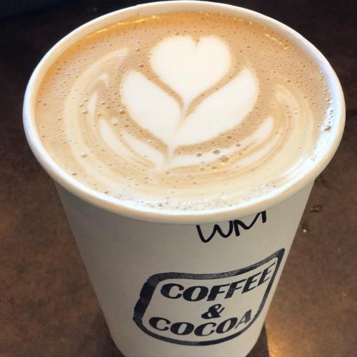 A latte in a white cup with a heart-shaped foam design, placed on a wooden surface.