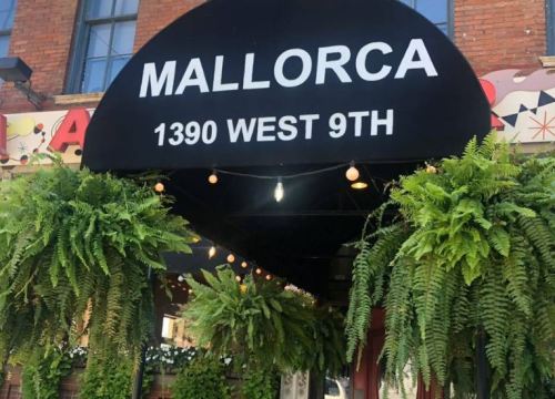 A storefront awning reading "MALLORCA 1390 WEST 9TH" adorned with hanging ferns and string lights.