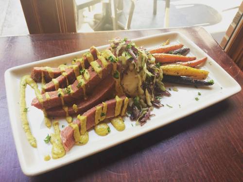 A plate of sliced meat with mustard sauce, mashed potatoes, and colorful roasted carrots, garnished with herbs.