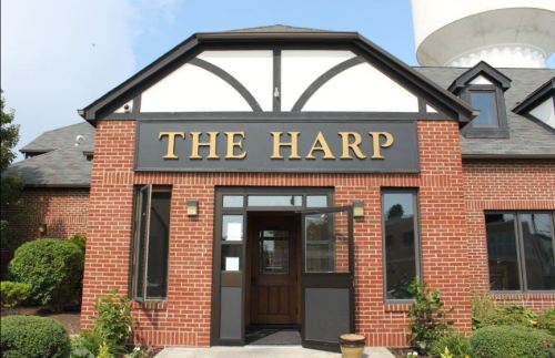 Exterior of a brick building with a sign reading "THE HARP," featuring a welcoming entrance and landscaped surroundings.