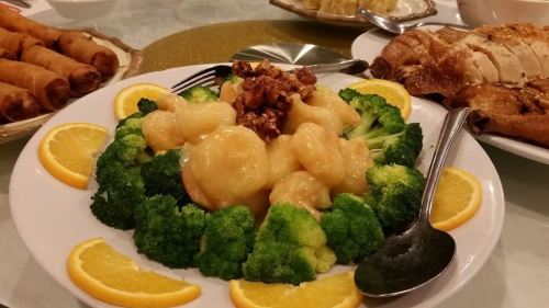A plate of shrimp with a creamy sauce, surrounded by broccoli and garnished with orange slices and walnuts.