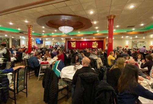 A bustling restaurant filled with diners at tables, decorated with red accents and festive decor.
