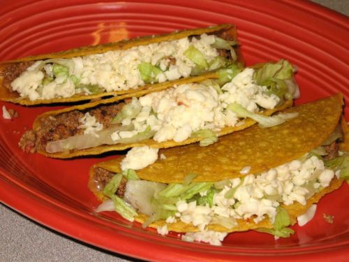 Three crunchy tacos filled with seasoned meat, lettuce, and cheese on a red plate.