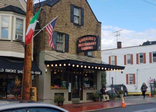 A brick building with a sign for Guarino's Restaurant and Liquors, featuring flags and string lights outside.