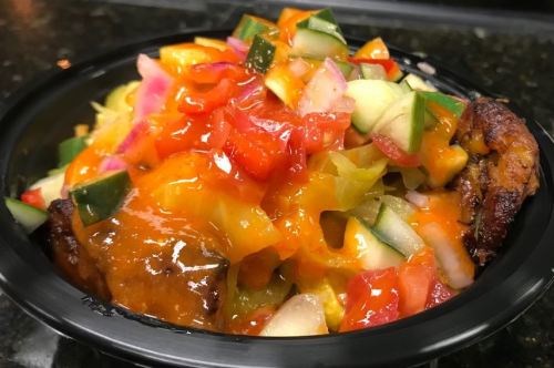 A colorful bowl filled with grilled meat, fresh vegetables, and a drizzle of sauce, served in a black container.