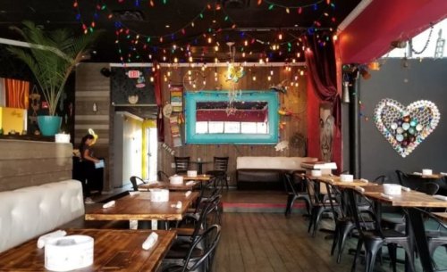 Cozy restaurant interior with wooden tables, colorful lights, and vibrant decor, featuring a heart made of bottle caps.
