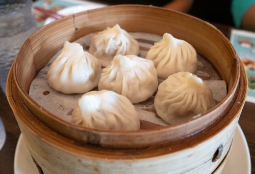 A bamboo steamer filled with eight freshly steamed dumplings, resting on a plate.