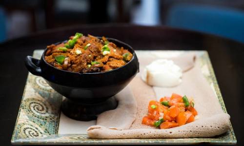 A bowl of spicy meat stew with green peppers, served with a side of fresh tomato salad and a dollop of yogurt.