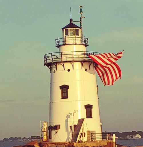 A white lighthouse with a red and white striped flag waving in the breeze against a soft sunset sky.