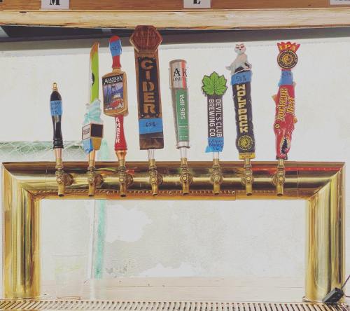 A row of colorful beer taps with various labels, set against a golden tap handle at a bar.