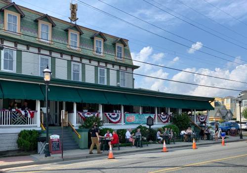 A historic building with a green awning, outdoor seating, and patriotic decorations, set against a blue sky.