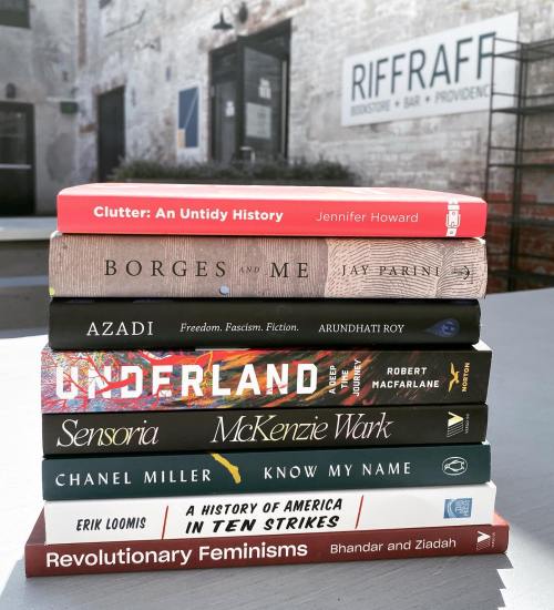 A stack of books on a table outside a bookstore, featuring titles like "Clutter," "Azadi," and "Know My Name."