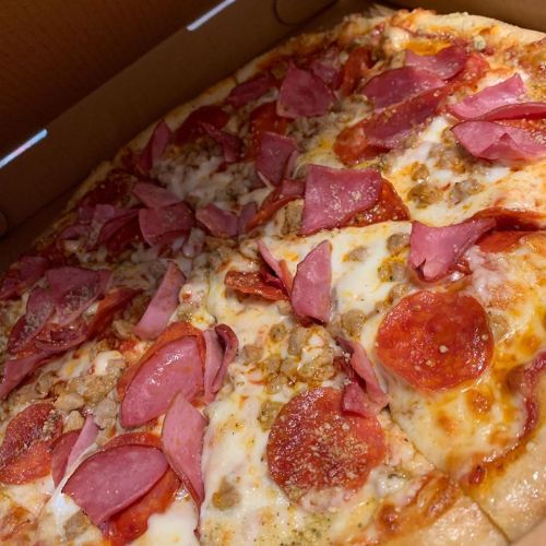 A close-up of a pizza topped with pepperoni, ham, and sausage, inside a pizza box.