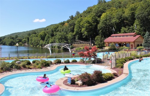 A scenic water park with lazy river, colorful inner tubes, and lush green trees by a lake under a clear blue sky.