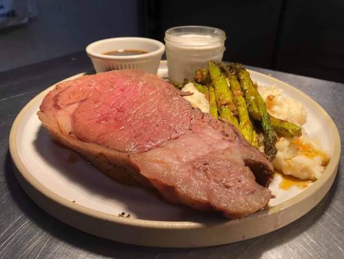 A plate with a slice of roast beef, mashed potatoes, grilled asparagus, and dipping sauces.