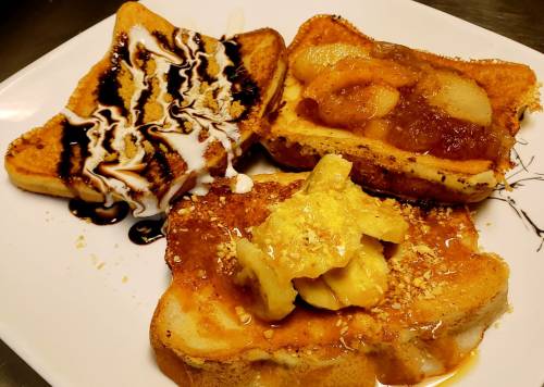 Three slices of French toast topped with fruit, syrup, and drizzles on a white plate.