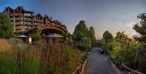 A scenic view of a hotel surrounded by vibrant gardens and flowers, with a sunset in the background.