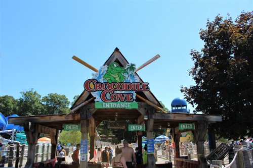 Entrance to Crocodile Cove water park, featuring a colorful sign and a sunny day with visitors enjoying the attractions.