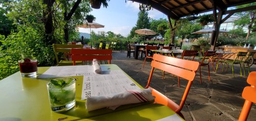 Outdoor dining area with colorful chairs, tables, and umbrellas, surrounded by greenery and a scenic view.