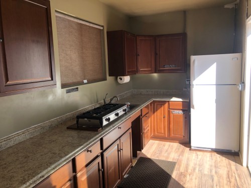 Bright kitchen with wooden cabinets, a gas stove, and a white refrigerator, featuring a countertop and window shades.