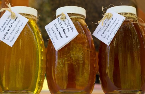 Three jars of honey labeled "Spring Wildflower," "Black Dirt Blossom," and "Orange Blossom," displayed with twine tags.