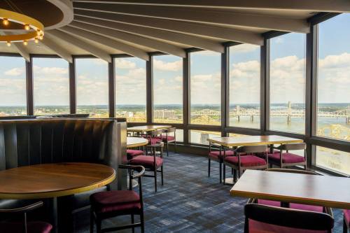 A modern restaurant interior with round tables and chairs, featuring large windows overlooking a river and bridge.