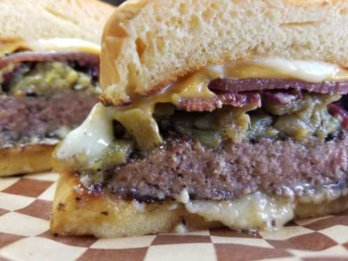 Close-up of a juicy burger with melted cheese, bacon, pickles, and sauce, served on toasted bread.