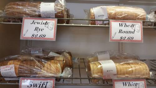 Loaves of bread in clear packaging on shelves, labeled Jewish Rye, Wheat Round, Swift, and White, each priced at $2.69.