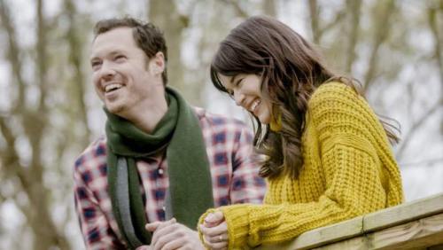 A smiling couple in a park, enjoying each other's company while wearing cozy sweaters.