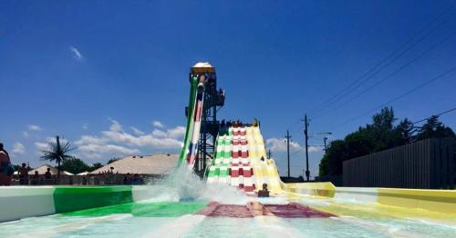A colorful water slide at a water park with people sliding down and splashing into the pool below under a clear blue sky.