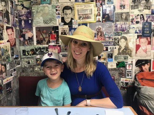 A woman in a wide-brimmed hat sits with a young boy in a restaurant decorated with various photos and memorabilia.