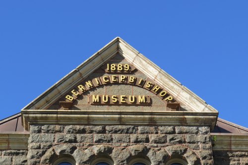 Sign on a historic building reads "1889 Bernice P. Bishop Museum" against a clear blue sky.