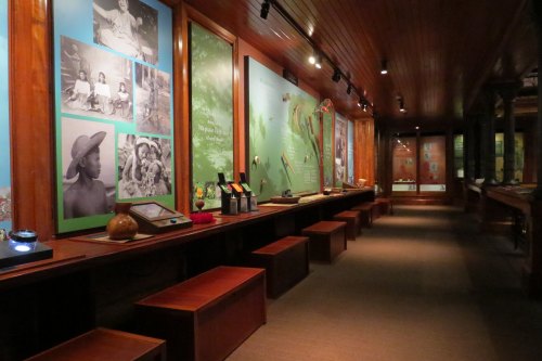 A museum exhibit featuring wooden benches, informational panels, and artifacts in a warmly lit hallway.