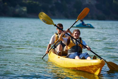 Two boys paddle a yellow kayak on a calm lake, enjoying a sunny day outdoors.
