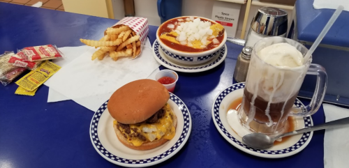 A table with a cheeseburger, chili cheese fries, a root beer float, and a side of fries with condiments.