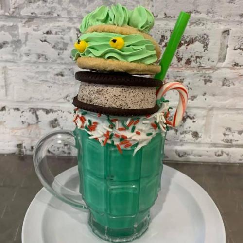 A tall glass filled with green milkshake, topped with a cookie monster cookie, Oreo, and festive sprinkles.
