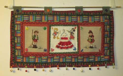Colorful wall hanging featuring three embroidered panels with playful characters and decorative borders.