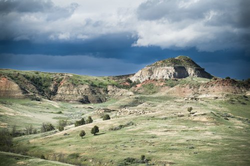 A scenic view of rolling hills and a prominent rock formation under a cloudy sky.