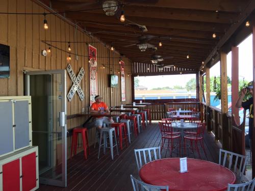 Outdoor dining area with wooden walls, string lights, and metal tables. A person sits at the bar in the background.