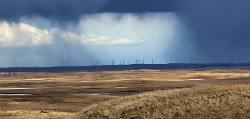 A vast landscape with rolling hills, wind turbines in the distance, and dark storm clouds looming overhead.