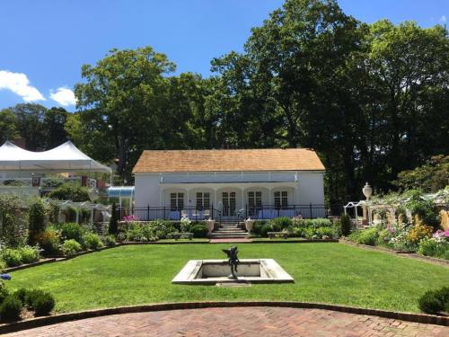 A charming white building surrounded by lush gardens and a fountain, under a clear blue sky.