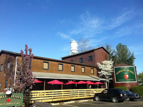 A rustic restaurant with a wooden exterior, red umbrellas on the patio, and a water tower in the background under a blue sky.