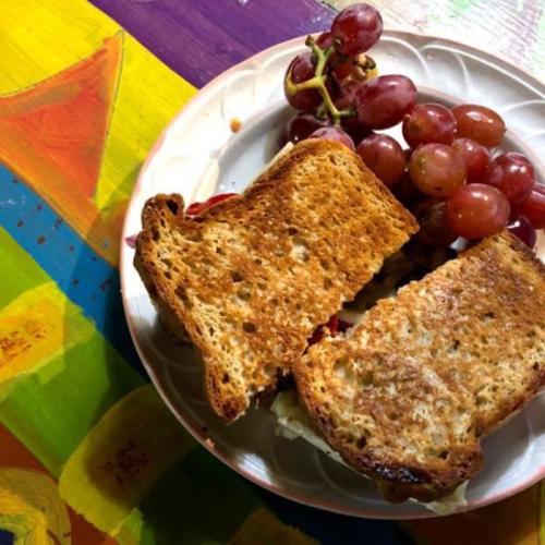 A plate with a toasted sandwich and a bunch of grapes, set against a colorful, painted background.
