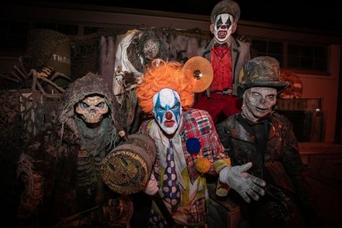 A creepy clown surrounded by eerie, skeletal figures and ghoulish characters in a dark, spooky setting.