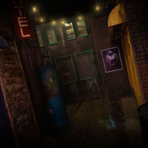 Dimly lit alleyway with brick walls, a yellow door, green windows, and barrels, creating a moody, urban atmosphere.