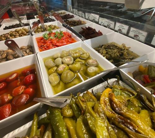 A variety of colorful dishes in white bowls, including olives, pickled vegetables, and peppers, displayed on a buffet.