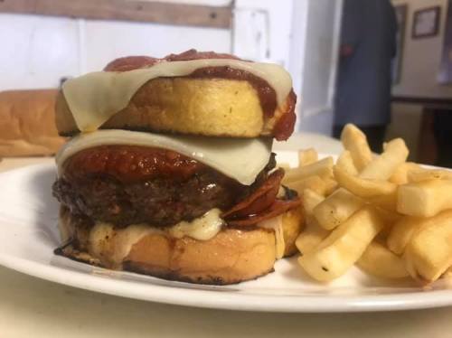 A towering burger with melted cheese and sauce, served with a side of golden fries on a white plate.